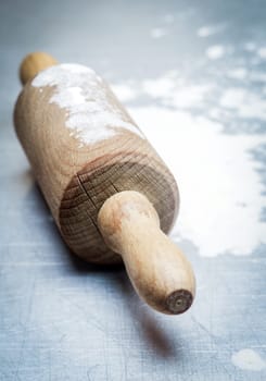 Old wooden rolling pin with scattered flour on a blue kitchen surface during baking of homemade pastries or pizza