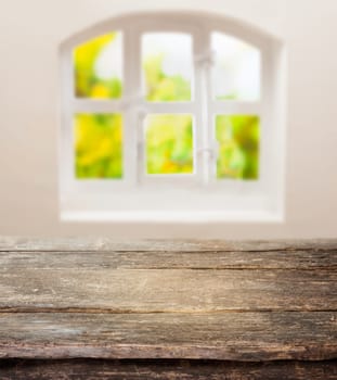 Old grunge table with a weathered rustic wooden top in front of a sunny cottage pane window in a country kitchen with space for your ingredients or product