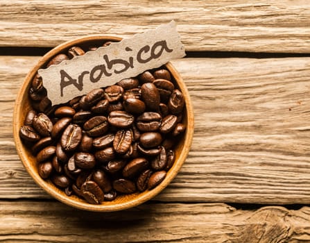 Bowl full of Arabica coffee beans over an old wooden table