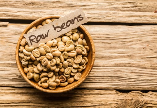 Bowl of raw coffee beans over an old wooden table