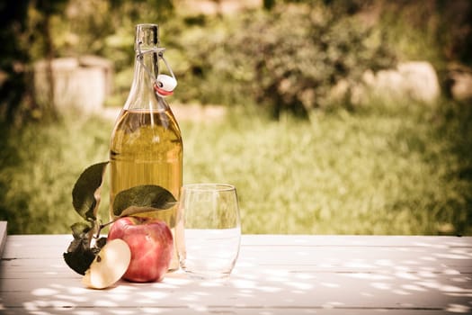Bottle of refreshing apple juice squeezed from fresh apples harvested in the garden standing outdoors on a rustic wooden table