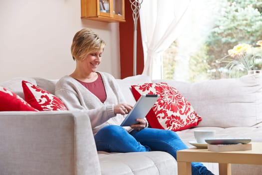 Mother enjoying surfing on the net with tablet  while relaxing at home with coffee