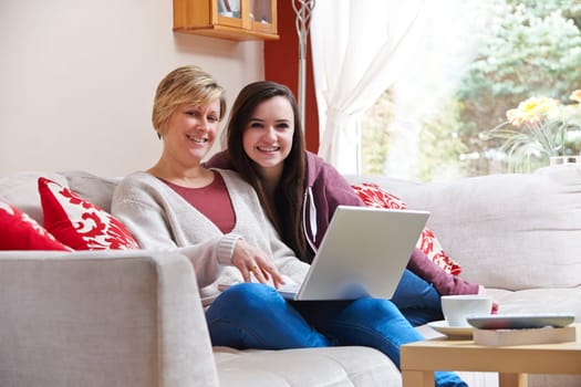 Mother and daughter enjoying surfing on the net while relaxing at home with coffee