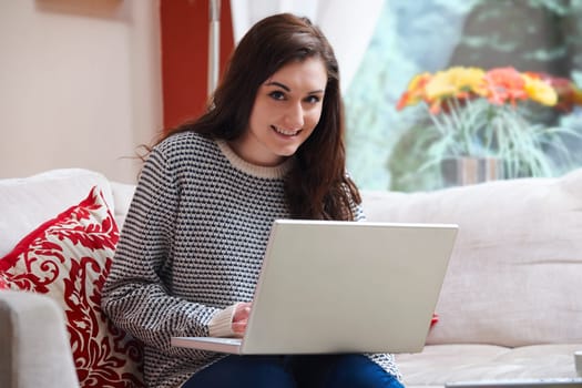 teenage girl smiling at camera while on laptop at home
