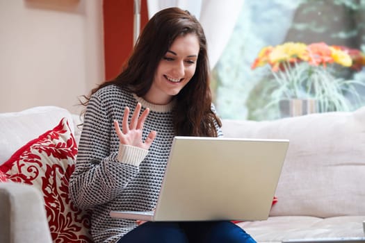 teenage girl waving at laptop while using webcam at home