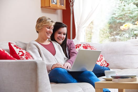 Mother and daughter enjoying surfing on the net while relaxing at home with coffee
