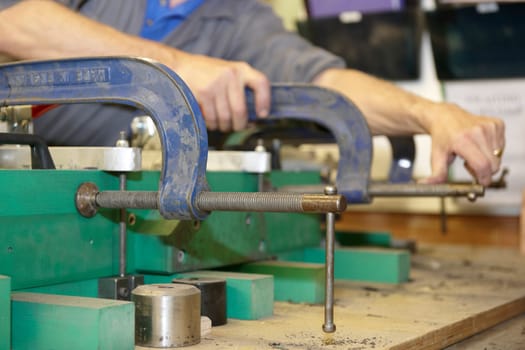 worker on factory floor tightening clamps to secure a machine