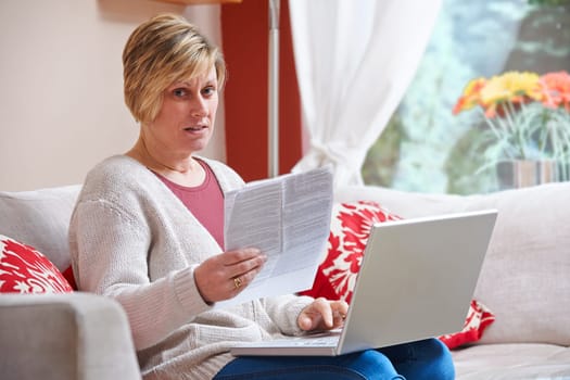 Woman looking happy while sitting at home doing home banking with laptop