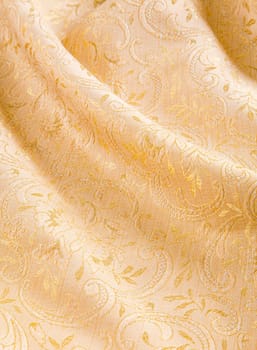 Soft folds of draped gold damask with a shiny floral pattern for a luxurious background of textiles used for interior decorating