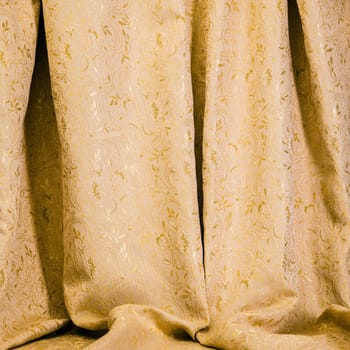 Background texture of drapes of golden damask material with a shiny self patterning of flowers and acanthus leaves hanging in luxuriant soft folds for an elegant interior decor