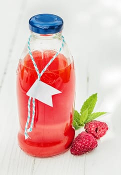 Homemade fresh raspberry juice in a glass bottle made from freshly squeezed fruit together with two fresh berries on a rustic white wooden background