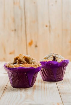 Two freshly baked healthy muffins with muesli and nuts in colourful purple paper cups for a healthy breakfast or teatime snack