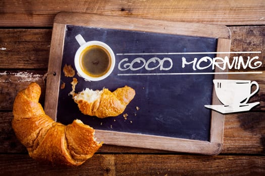 Good morning sign with a cup of fresh hot morning coffee and a broken croissant on an old school slate with a distressed wooden frame on a rustic table