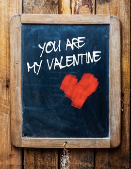 Vintage style chalkboard over old wood background, with the message You are my Valentine written in white chalk next to a red chalk heart