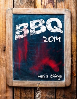 BBQ advertised on an old vintage school slate in a grunge wooden frame on a rustic table with an addendum at the bottom saying - Mans stuff