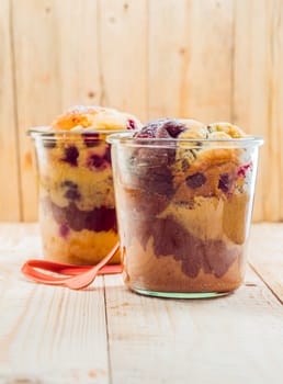 Close-up of two glasses with tasty vanilla and chocolate homemade fruitcakes, on a wooden table