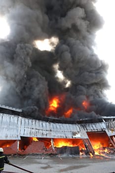Warehouse building burning with intense flames and fireman attending