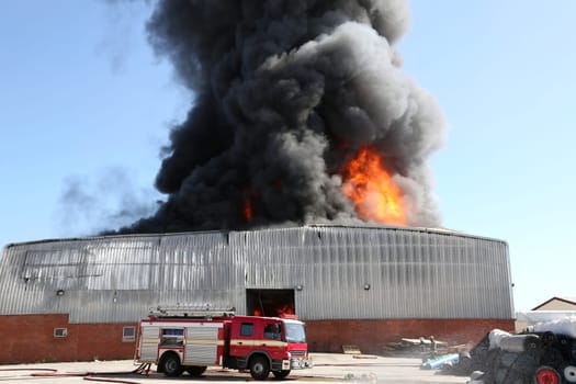 Warehouse building burning with intense flames and firemen attending