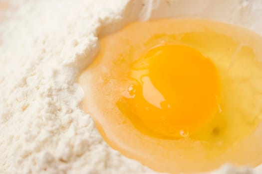 Flour on a wooden cutting board with a egg in the middle of it.