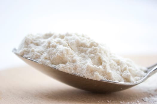 Metal spoon full with flour on a wooden cutting board.