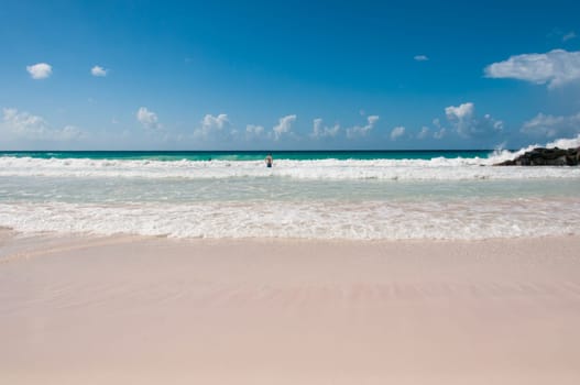Blick auf das Meer an einem karibischen Traumstrand mit drei badenden Personen und viel Strandfläche im Vordergrund.
