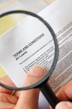 hands holding magnifying glass reading terms and conditions of loan agreement