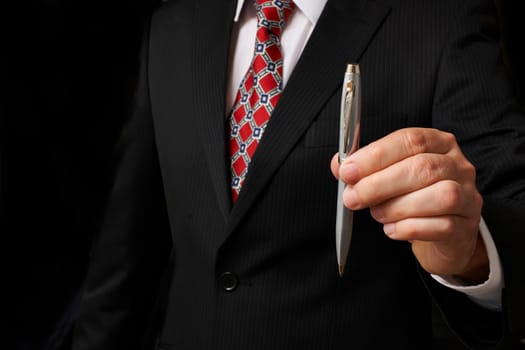 businessman in suit holding out pen towards camera
