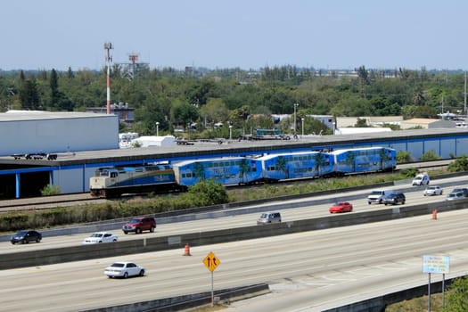 FORT LAUDERDALE, FLORIDA - MARCH 30, 2013: Tri-Rail engine and three passenger trains moving south next to I-95 Highway. This public transportation links three counties from Mangonia Park to Miami.
