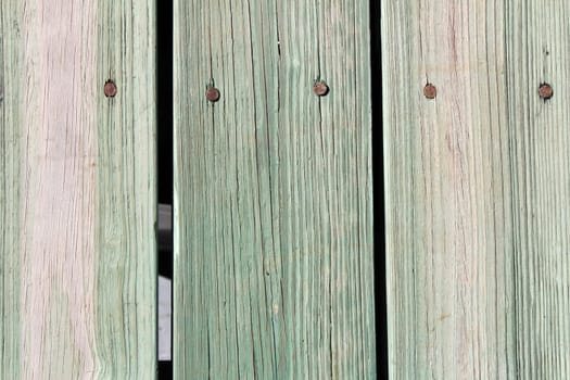 Closeup of nailed green tan wooden slats that make up an outdoor sidewalk on a sunny day..
