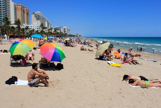 FORT LAUDERDALE, FLORIDA - APRIL 8, 2013: Colorful Atlantic coast beach scene of many people suntanning, relaxing and enjoying the shore during spring break on a hot and sunny, clear blue sky day.