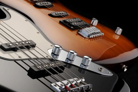 a close up of a electric guitar , and  of a black bass glossy on dark background