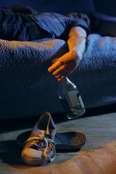 Young drunk man, lying on the couch with a bottle in hand