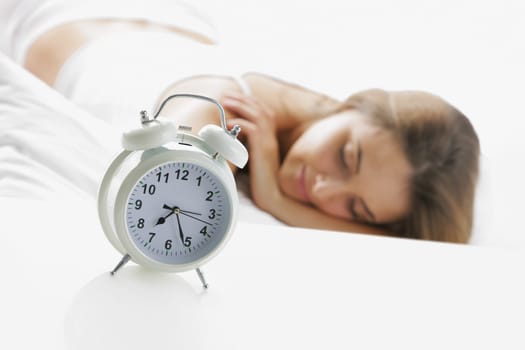 A young lady sleeping on the background with a clock on the foreground.