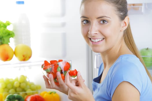 Smiling girl with strawberries near the refrigerator