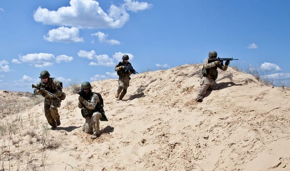 Squad of soldiers run through the desert through the military operation