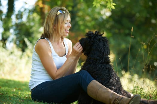 woman relaxing with black dog while on a walk in the park