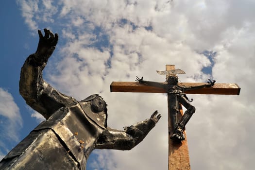 Modern steel statue of Christ with Virgin Mary lying at his feet against blue sky