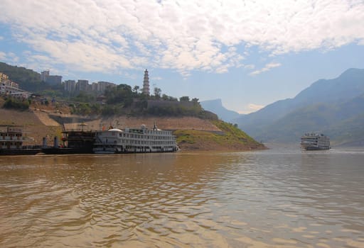 A view of the Yangtse river with river cruise boats for tourists and a pagoda on a hill.