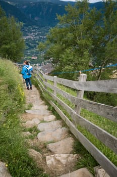 Vanishing point view of the Merano high-altitude hiking trail with woman on a slope section above the village of Tyrol in South Tyrol in summer 2013