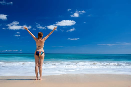 Beautiful young woman with arms open in a tropical beach enjoying the summer