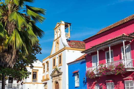 Historic white colonial church standing next to blue and pink historic buildings in Cartagena, Colombia