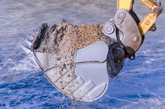 Excavator bucket dredging sand and gravel from the seafront