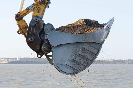 Excavator bucket dredging sand and gravel from the seafront