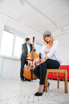 Woman on stool with microphone and man plays