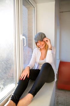 Young woman on windowsill smile and touch hat