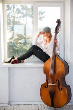 Charming woman with hat on windowsill and contrabass