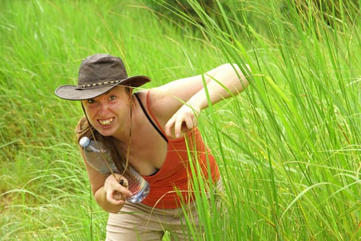 A caucasian woman hides in long jungle grass pretending to be a scary animal