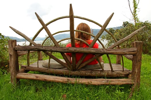 A woman stops to rest on a large wooden bench in the woods on a lake shore