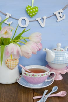 Fresh tea in a colourful cup and tulips in a vase