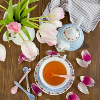 Fresh tea in a colourful cup and tulips in a vase